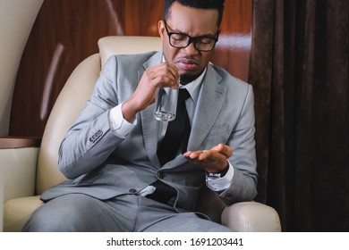 Nervous African American Businessman Taking Pills While Having Nausea Or Panic Attack During Flight On Private Plane