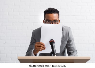 Nervous African American Speaker Hiding Behind Paper During Business Conference