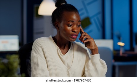 Nervous african manager discussing at smartphone with employee working overtime sitting at desk in business office late at night resolving financial problem. Furious businesswoman overworking