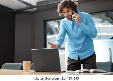 Nervous Business Man Talking On Cellphone Standing In Front Of Laptop At Office, Fighting With Clients Or Colleagues, Gesturing And Yelling Looking At Pc Screen, Frustrated Boss Speaking With Employee