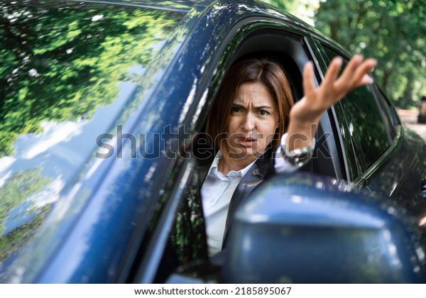 Nervous business woman driving and peeps out\
of the window of her luxury car. Discontented woman in black suit\
standing in traffic jam and looking out of her car and\
demonstrating her\
displeasure