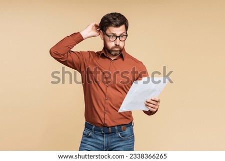 Nervous businessman missed deadline. Portrait of emotional middle aged student man wearing eyeglasses holding documents, reading information isolated on beige background