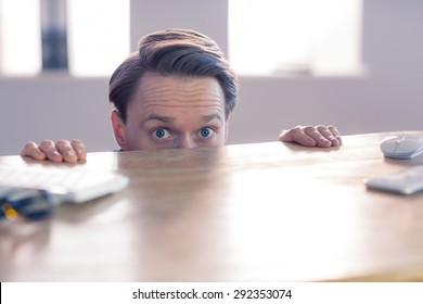 Nervous businessman peeking over desk in his office