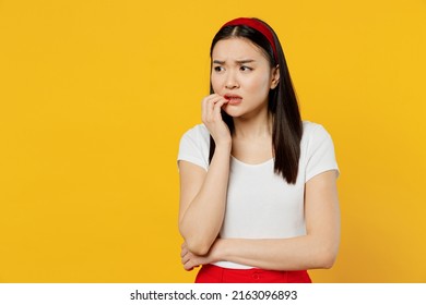 Nervous Disturb Young Sad Woman Of Asian Ethnicity 20s Years Old Wears White T-shirt Looking Aside Biting Nails Isolated On Plain Yellow Background Studio Portrait. People Emotions Lifestyle Concept