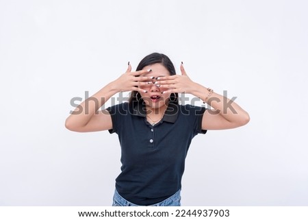 A nervous but excited young asian woman tries to cover her eyes, anticipating a happy surprise. Isolated on a white background. Spoiler alert concept.