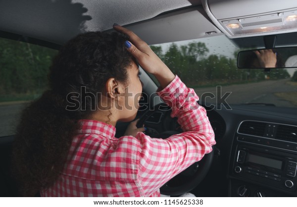 Nervous female driver sits at wheel, has\
worried expression as afraids to drive car by herself for first\
time. Frightened woman has car accident on road. People, driving,\
problems with transport