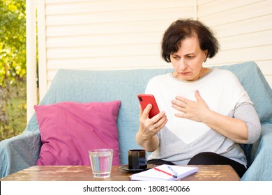 Nervous Frustrated Brunette Senior Woman Holding Mobile Phone And Looking At Screen While Reading Disturbing News In Media, Watching Shocked Video Content, Sitting On Sofa On Home Terrace Outdoors