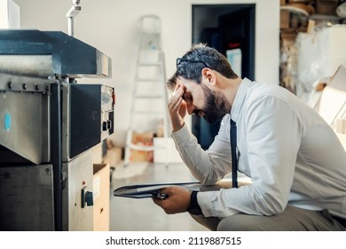 A nervous graphic engineer crouching next to printing machine with malfunction at printing shop.