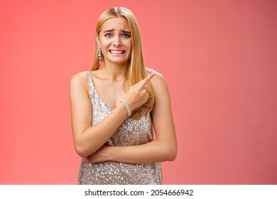 Nervous Hesitant Attractive Worried Blond Woman Cringing Frowning Clench Teeth Pointing Behind Seek Friends Help See Ex-boyfriend Unwilling Be Seen, Standing Anxious Awkward Party Red Background