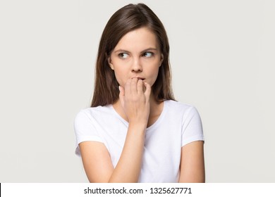 Nervous insecure young woman looking aside feeling fear uncertainty worried scared biting nails, stressed shy doubtful teen girl student anxious about problem isolated on white grey studio background