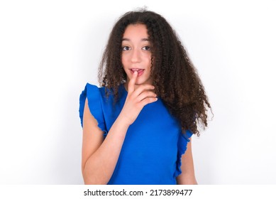 Nervous puzzled Teenager girl with afro hair style wearing blue t-shirt over white background opens mouth from surprise, reacts on sudden news.