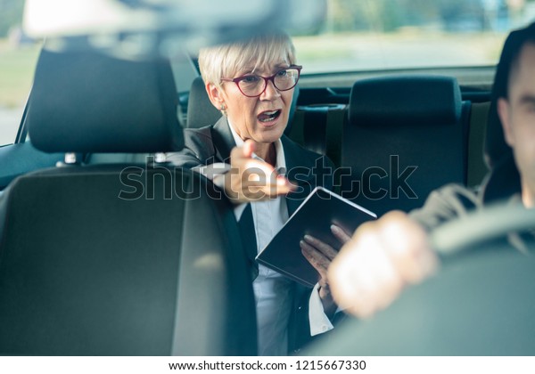 Nervous senior\
female manager riding on a back seat of a car, running late for a\
meeting, shouting at her\
driver