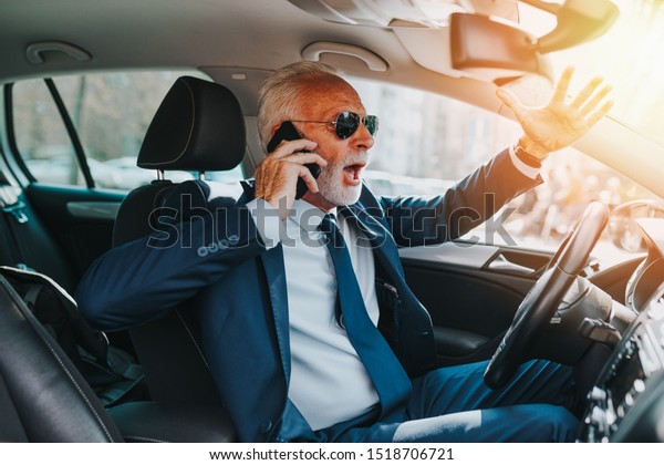 Nervous\
senior good looking businessman getting angry and nervous while\
talking on mobile phone and driving his\
car.