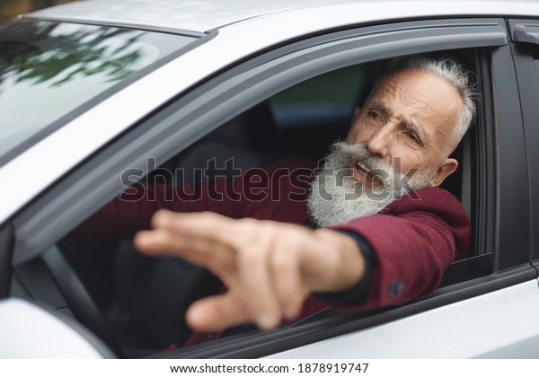Nervous senior man driver fighting on the road,\
stuck in traffic, side view. Stressed aged grey-haired businessman\
yelling and gesturing while driving car, going for business\
meeting, free space
