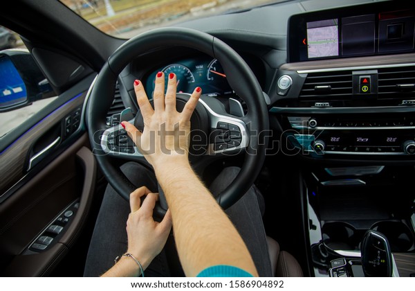 nervous situation on the road concept. woman\
with her right hand presses horn on the steering wheel and drives a\
modern car with a black interior. girl rides in her car.close-up,\
blur background