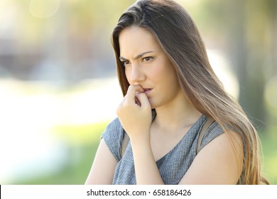 Nervous woman biting nails and looking away alone outdoors in the street