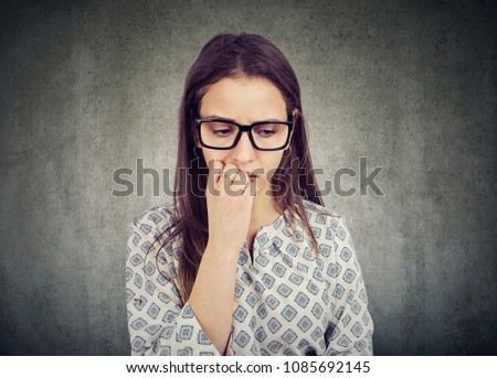 Nervous woman biting nails and looking down feeling insecure 