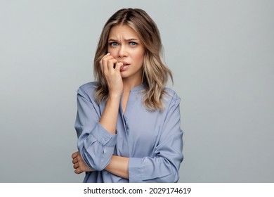 Nervous woman feeling insecure afraid and anxious biting nails from worries and stress. Studio portrait of young blond female businesswoman frustrated stressed and confused scared of problems at work