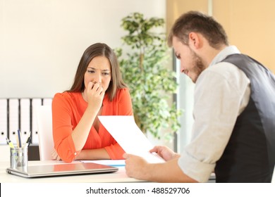 Nervous Woman Looking At Manager Reading Her Resume During A Job Interview At Office