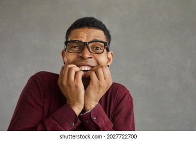 Nervous young african american man biting fingers close up face portrait shot on grey wall copy space. Black guy feeling fear, scary and stress emotion. Overwhelmed and terrified people reaction - Shutterstock ID 2027722700