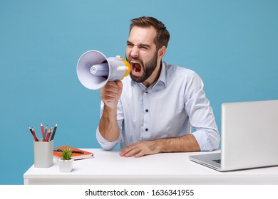 Nervous Young Bearded Man In Light Shirt Sit Work At Desk With Pc Laptop Isolated On Pastel Blue Background. Achievement Business Career Concept. Mock Up Copy Space. Scream In Megaphone Looking Aside