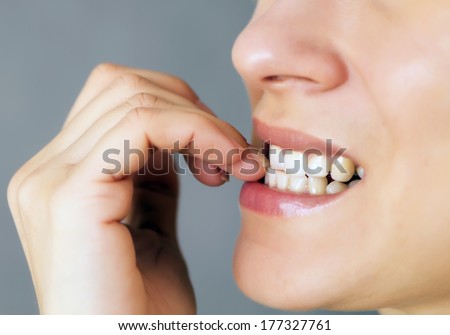 nervous young woman biting her nails on gray background