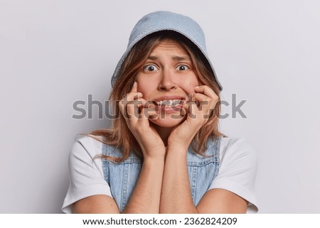 Nervous young woman looking guilty or worried being scared of something wears denim panama casual t shirt and vest isolated over white background. People reactions and negative emotions concept