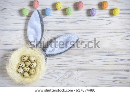 A nest with colored Easter eggs and bunny ears at home on Easter day. Celebrating Easter at spring. Painting eggs. Wooden background
