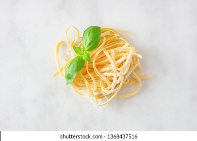 Nest Of Fresh Linguine Pasta With Basil. Top View Against A White Marble Background.