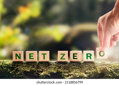 Net zero 2050 Carbon neutral. Net zero greenhouse gas emissions target. Climate neutral long strategy. No toxic gases. Hand puts wooden cubes with netzero icon in green background copy space.