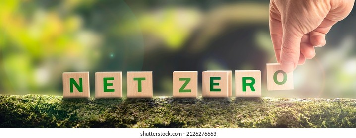 Net zero by 2050 Carbon neutral. Net zero greenhouse gas emissions target. Climate neutral long strategy. No toxic gases. Hand puts wooden cubes with netzero icon in green background panoramic - Shutterstock ID 2126276663