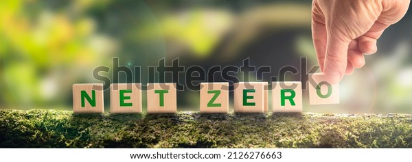 Net zero by 2050 Carbon neutral. Net zero\
greenhouse gas emissions target. Climate neutral long strategy. No\
toxic gases. Hand puts wooden cubes with netzero icon in green\
background panoramic