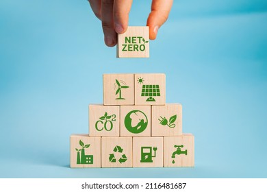 Net zero and carbon neutral concept. Net zero greenhouse gas emissions target. Climate neutral long term strategy. Hand put wooden cubes with green net zero icon and green icon on grey background.