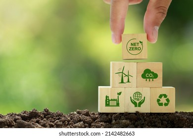 Net zero and carbon neutral concept. Hand puts wooden cubes with netzero icons - renewable energy, co2 emissions reduction, green production, waste recycling.in green background   - Shutterstock ID 2142482663