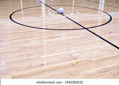 Netball Ball. An Eye Level Long Shot Of A Netball Ball Placed In The Centre Circle On An Indoor Netball Court Which Is Made Of Wooden Floorboards.