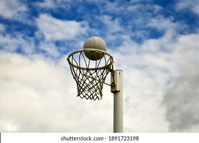 A Netball Ball Positioned Just Above The Rim Of A Netball Hoop.