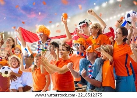 Netherlands football supporter on stadium. Dutch fans on soccer pitch watching team play. Group of supporters with flag and national jersey cheering for Holland. Championship game. Hup Holland