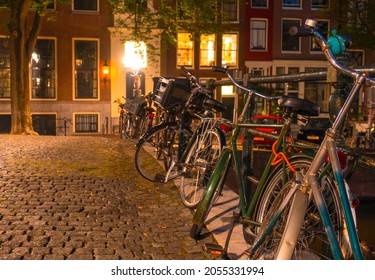 Netherlands. Night Amsterdam. Several bicycles are parked at the canal fence on the cobbled pavement