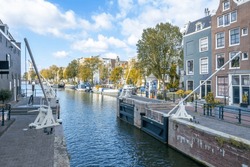 Netherlands. Old Ship Gateway On The Amsterdam Canal. Typical Dutch Houses And Residential Barges On The Water