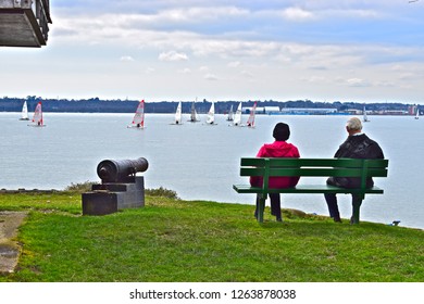 Netley, Hampshire / England -4/1/2018: A Older Couple Relaxing On A Seat At Weston Sailing Club And Watching Distant Dinghy Racing On Southampton Water.