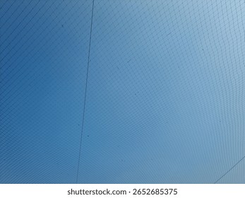 Netting pattern stretched with blue sky background, showing geometric lines and texture detail in outdoor lighting.