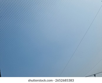 Netting pattern stretched with blue sky background, showing geometric lines and texture detail in outdoor lighting.