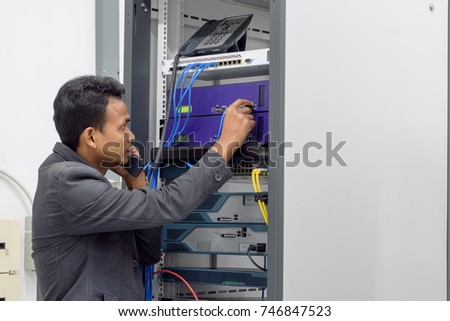 Network administrator talking on the ip phone and connecting utp cable to the network in 
 datacenter room