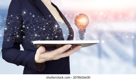 Network bright idea with light bulb. Hand hold white tablet with digital hologram light bulb sign on light blurred background. Business start up or goal to success
