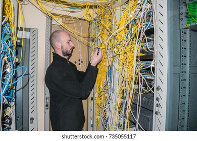 A network engineer connects two patch cord in the server room of the data center. A specialist works among the disorderly interweaving of Internet cables.  - Powered by Shutterstock