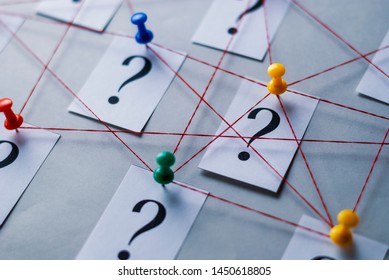 Network Of Printed Question Marks On White Cards Pinned With Thumb Tacks And Joined By String In A Conceptual Image Over A Grey Background