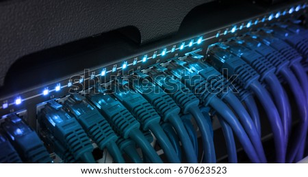 Network server panel, switch and patch cord cable in data center glowing in the dark. Blue led