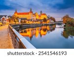 Neuburg an der Donau, Germany. Old town with Sclohss Neuburg and trees in autumn colors, Danube River water reflection, Bavaria beautiful small city.