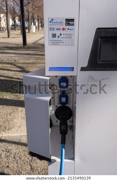 Neuf-Brisach, France - February 19 , 2022: A\
static shot of a solid black Tesla Model 3 dual motor long range\
awd charging at the AC Freshmile charging station in a sunny winter\
day. Selective\
focus.