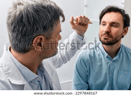 Neurologist doctor examining male patient, checking basic reflexes of human by shining flashlight into his eyes. Neurologist's consultation, neurology